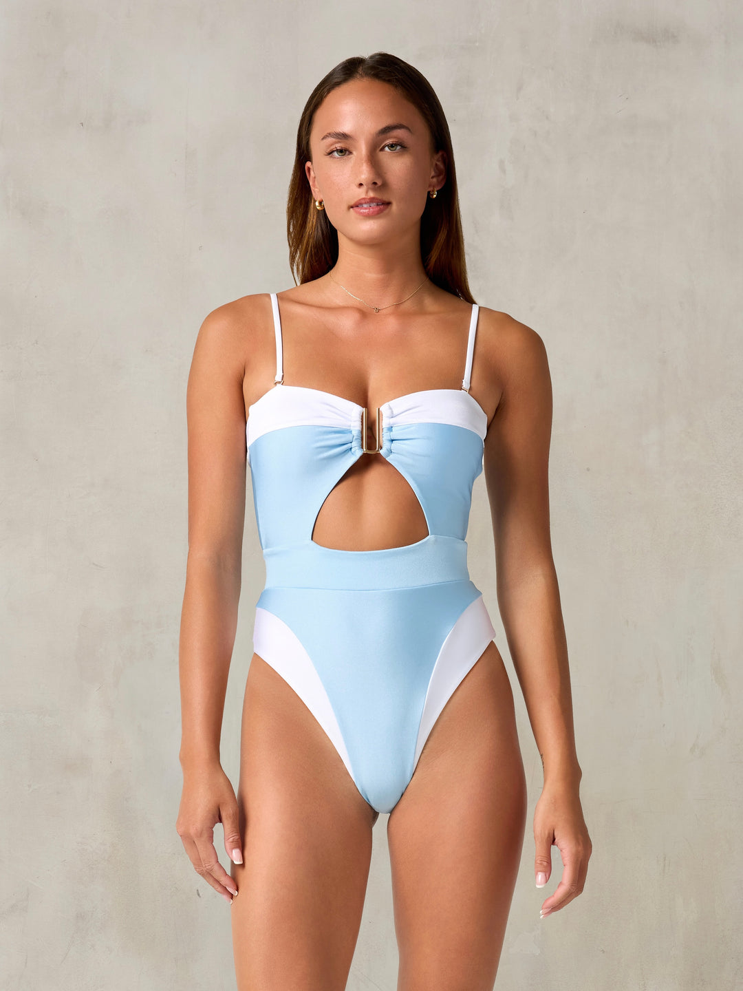 A model wearing a light blue and white one-piece swimsuit with a cut-out fr...